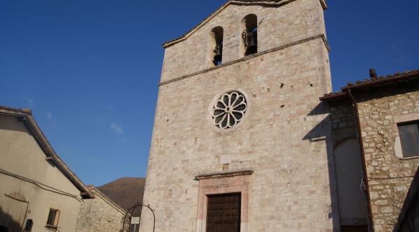  Façade en pierre de l’église Saint-Jean-Baptiste à Vallo di Nera, avec clocher-mur, rosace centrale et ciel dégagé. 