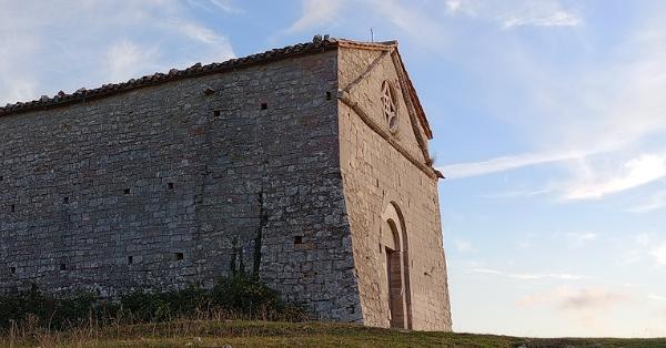  Side view of a stone building located on a grassy hill, with a blue sky and light clouds in the background. 