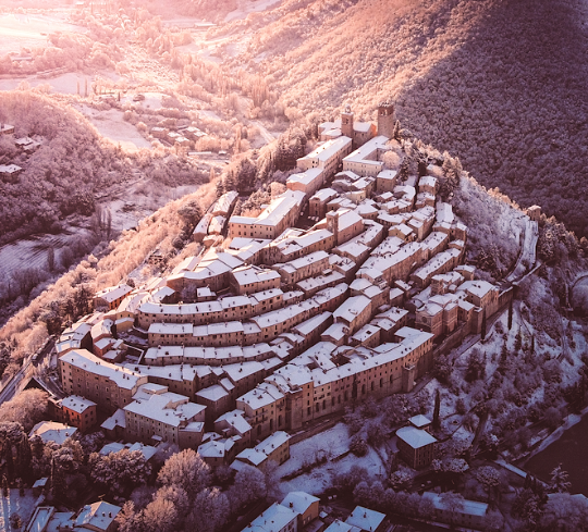  Aerial view of a medieval village blanketed in snow among hills bathed in the warm light of sunset. 